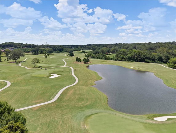 Panoramic view of a golf course with a lake and surrounding greenery.