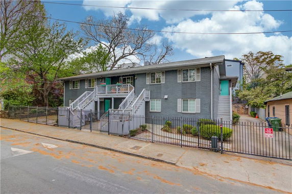 Front view of a two-story residential building with multiple entrances and a fenced yard.