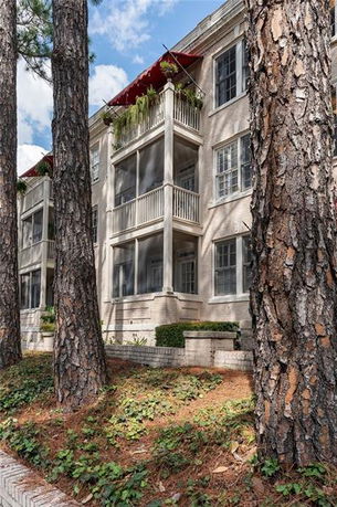 Front view of a multi-story building with balconies and large trees in front.