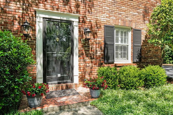 Front view of a brick house entrance with a glass door and window with shutters.