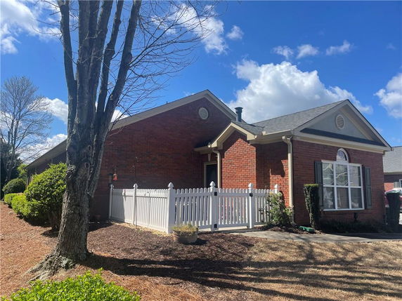 Front view of a single-story brick house with white fencing.