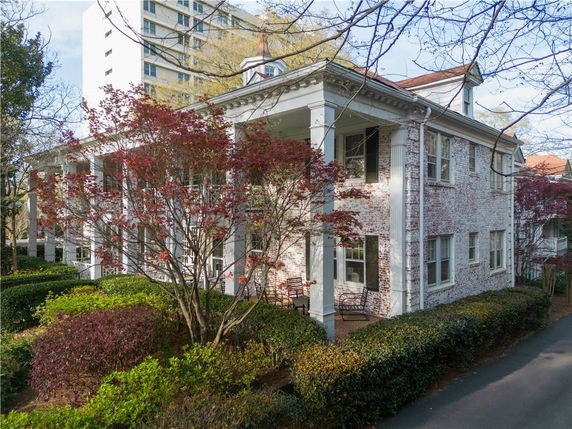 Corner view of a two-story brick house with porch columns and surrounding shrubbery.
