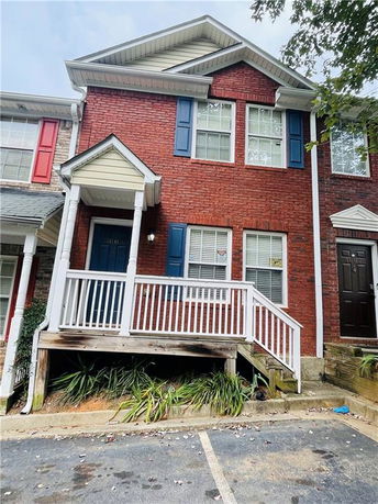 Front view of a brick two-story townhouse with white railings and blue shutters.