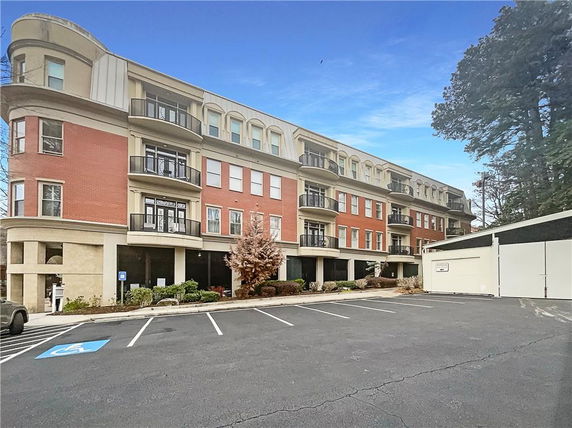 Front view of a multi-story building with balconies and a parking area.