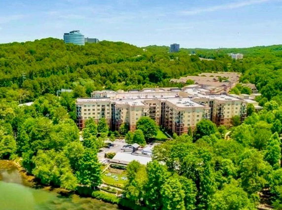 Aerial view of a large multi-story residential building surrounded by lush greenery and distant hills.