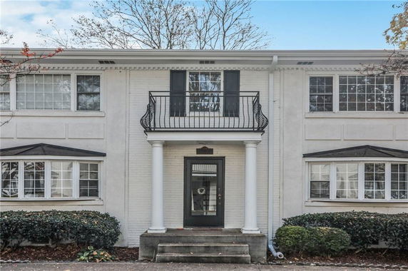 Front view of a two-story house with white brick exterior, flanked by columns and windows.