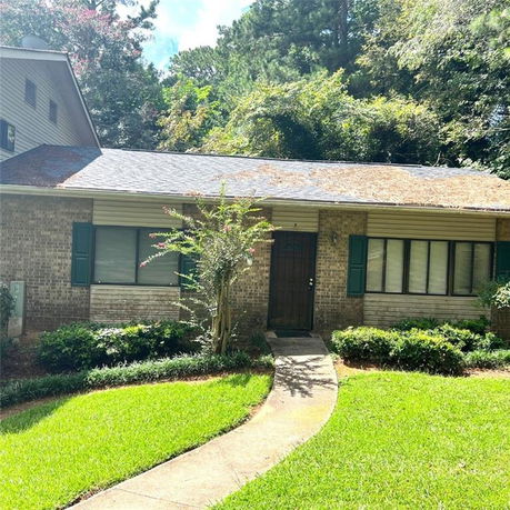 Front view of a single-story brick house with a shingled roof and green shutters.