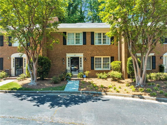 Front view of a two-story brick townhouse with black shutters and a small garden area.