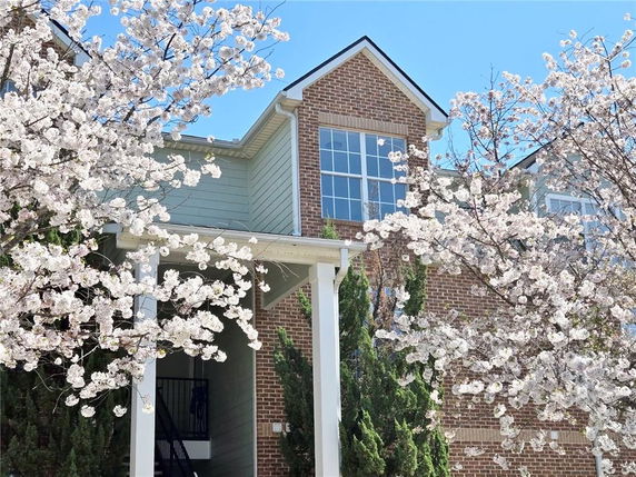 Front view of a two-story house with brick and siding exterior, visible through blooming trees.
