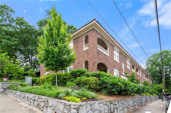 Front view of a brick two-story building with arched balconies and a landscaped stone retaining wall.