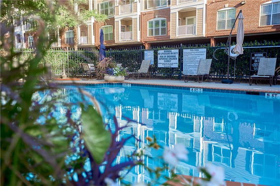 Outdoor swimming pool surrounded by apartment buildings with lounge chairs and umbrellas.