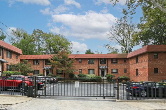 Front view of a multi-story brick apartment building with a gated parking area.
