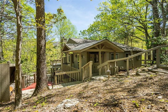 Front view of a small, rustic house surrounded by trees.