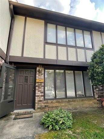 Front view of a two-story house with brick and stucco exterior, featuring large windows and a wooden door.
