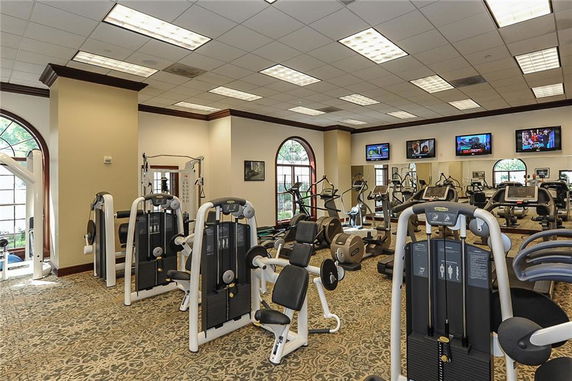 Indoor gym area with various exercise machines and televisions on the walls.