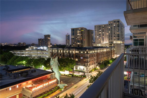 Panoramic view of a city skyline at dusk from a balcony, featuring tall buildings and street lights.