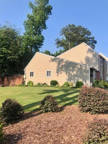 Side view of a multi-story house with beige siding and a sloped roof.
