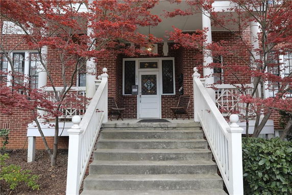Front view of a brick house with white railings and steps leading to the entrance.