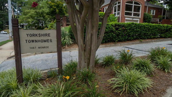 Front view of a townhouse with a surrounding garden and signage at the entrance.