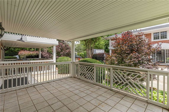 Covered patio area with railing and view of a brick building.