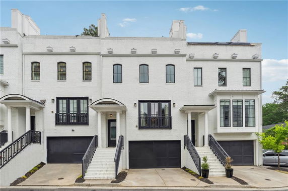 Front view of a row of three-story townhouses with black garage doors and white exterior brick walls.