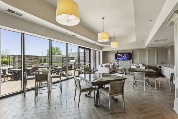 Interior of a club house with large windows, tables, chairs, and a TV on the wall.