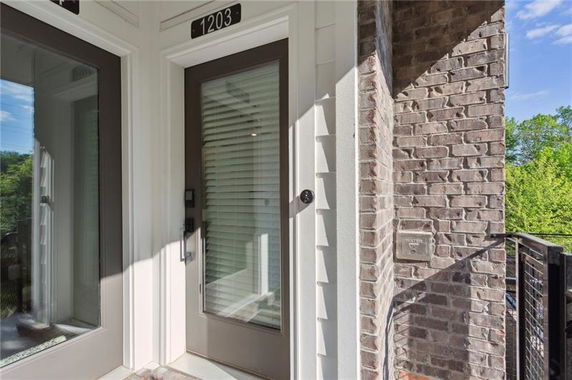 Front view of a door with glass panels and blinds, surrounded by brick and siding walls.