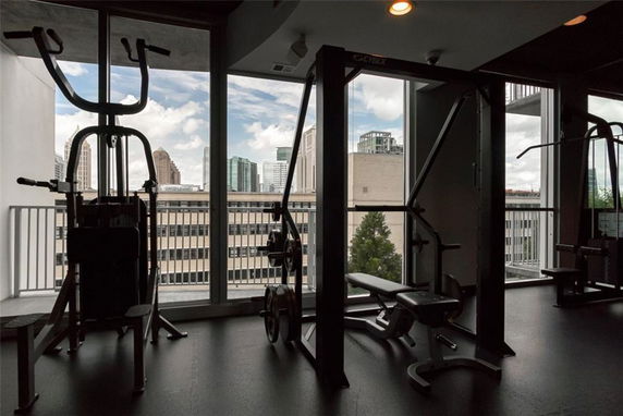 Interior view of a gym with exercise equipment and a large window showing a cityscape.