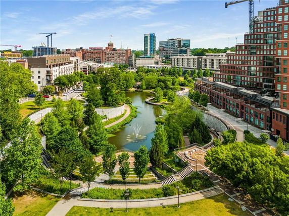 Aerial view of a landscaped park area with a pond and surrounding urban buildings.