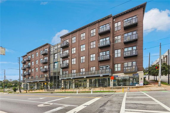 Front view of a multi-story brick building with balconies and ground floor shops.