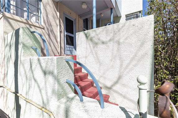 Entrance of a building with red steps and blue railings leading to a white door.