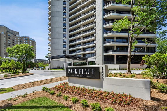 Front view of a multi-story building with balconies and a sign in front.