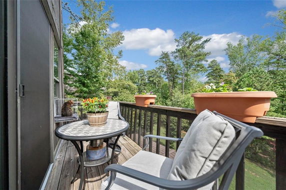 Outdoor balcony area with table, chairs, and potted plants, overlooking trees and sky.