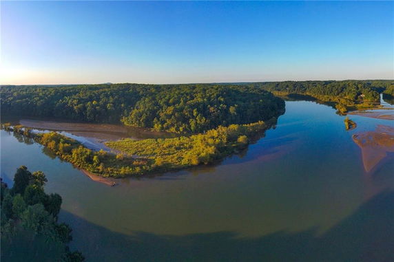 Aerial panoramic view of a river with surrounding forested areas under a clear blue sky.