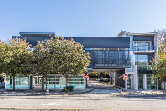 Front view of a modern multi-story building with large windows and an overhang design.