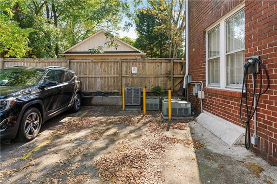 Outdoor parking area with a parked car and air conditioning units beside a brick building.