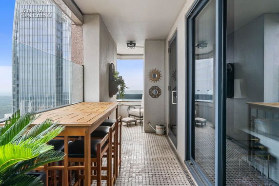 Balcony with table and stools, overlooking a cityscape and tall glass buildings.