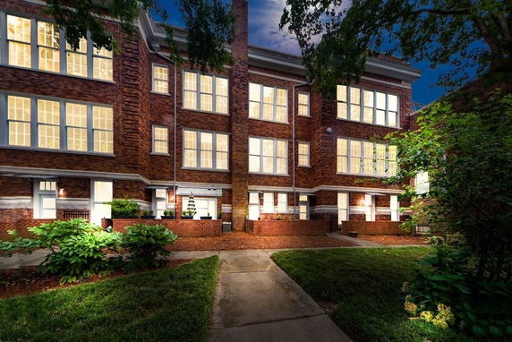 Front view of a multi-story brick building with numerous large windows lit up at night.