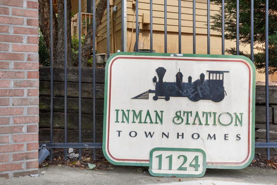 Entrance sign for Inman Station Townhomes with a train graphic, situated near a fence.