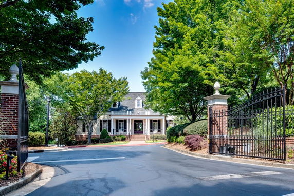 Front view of a large house with a gated entrance and surrounding trees.