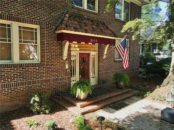 Front view of a two-story brick house with a red awning and American flag.
