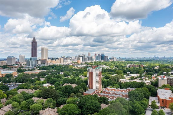 Panoramic view of a city skyline with numerous buildings and a lush green landscape.