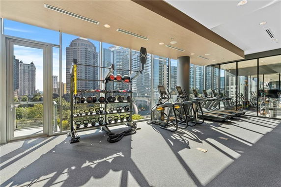 Indoor gym area with exercise equipment and glass windows overlooking city buildings.