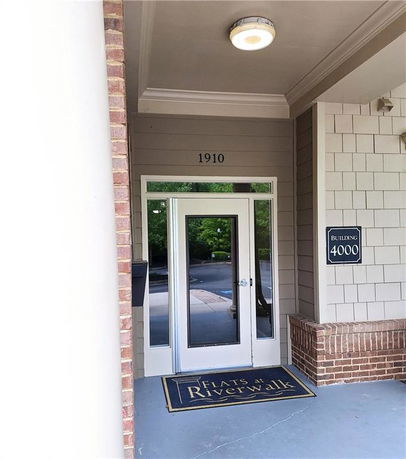 Entryway of a building labeled 'Flats at Riverwalk' with a glass door and brick accents.