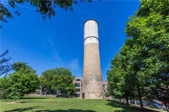 Tall cylindrical building structure with a narrow upper section against a clear blue sky.