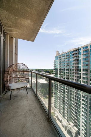 Balcony view from a high-rise building with a wicker chair and adjacent modern glass-building.