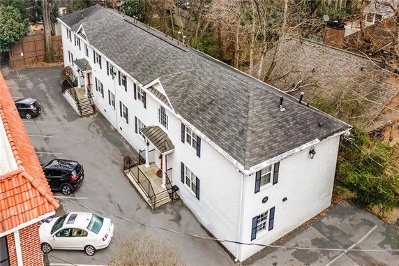 Aerial view of a two-story white building with a pitched roof and multiple entrances. The building has parking spaces in front.