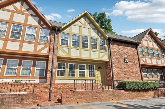 Front view of a multi-story house with brick and stucco exterior featuring large windows and a pitched roof.