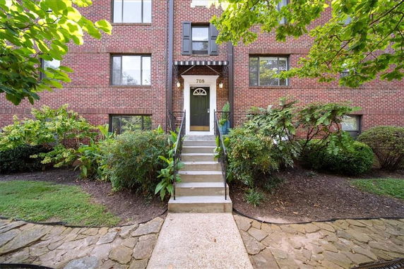 Front view of a brick apartment building with a central entrance and surrounding greenery.