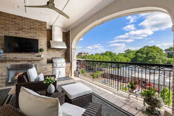 Covered outdoor area with seating, a grill, and a view of surrounding buildings and trees.